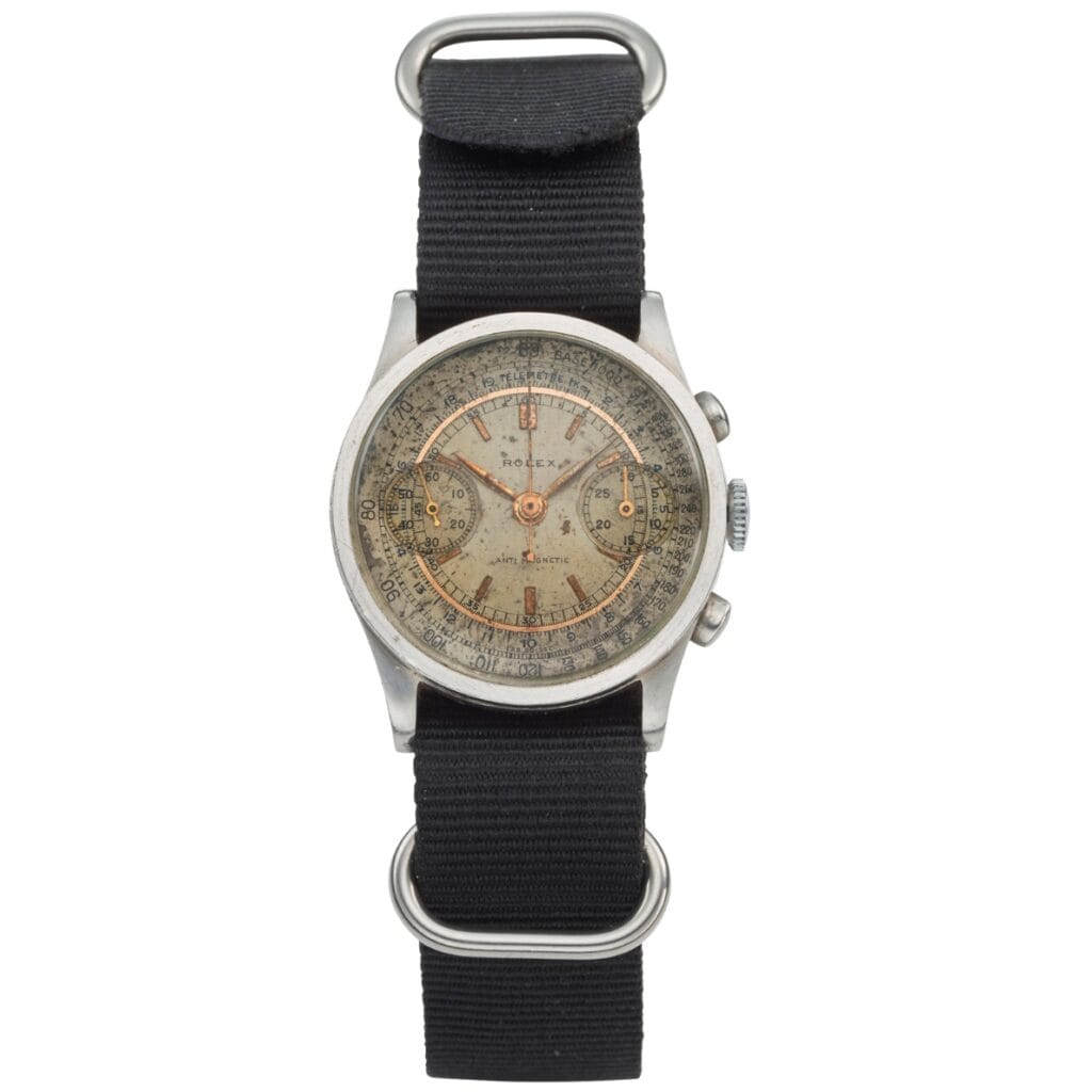 A vintage Rolex chronograph watch with a worn dial, black fabric strap, and classic 2811 movement.