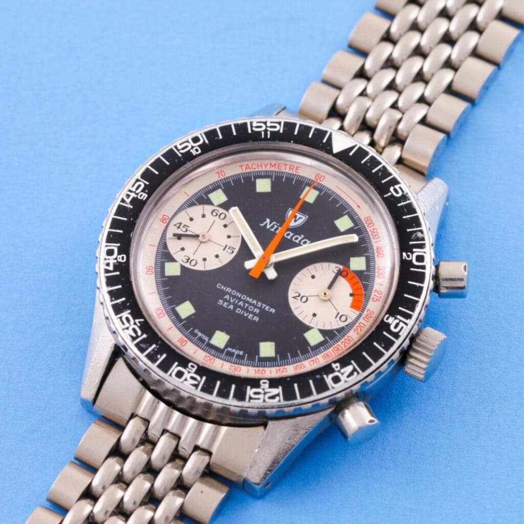 A vintage Nivada Grenchen Chronomaster Aviator Sea Diver chronograph wristwatch with a black dial and metal strap on a blue background.