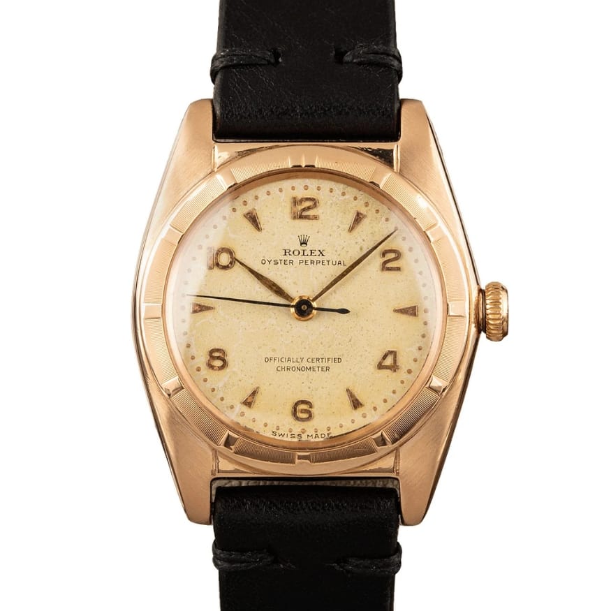 A vintage Rolex Oyster Perpetual 5011 watch with a gold case, cream dial, and black leather strap.