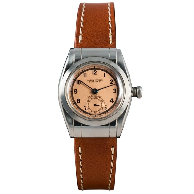 A vintage Rolex Oyster Perpetual wristwatch featuring a brown leather strap and a round, salmon-colored dial with black numerals. Model 3599.