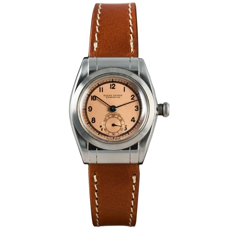 A vintage Rolex Oyster Perpetual wristwatch featuring a brown leather strap and a round, salmon-colored dial with black numerals. Model 3599.