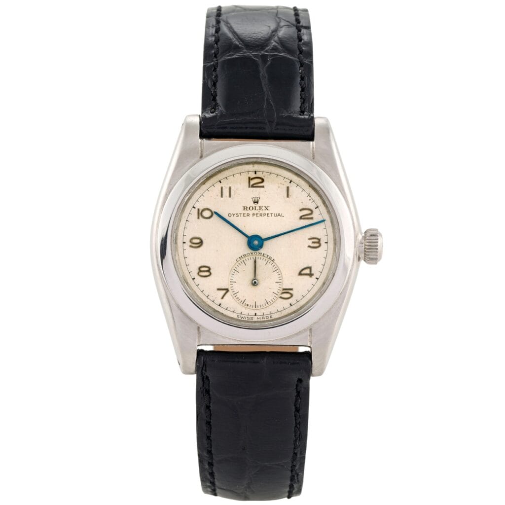 A vintage Rolex Oyster Perpetual 2764 watch with a black leather strap and a cream dial.