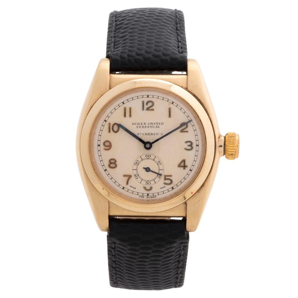 Vintage Rolex Oyster Perpetual wristwatch with a gold case, cream dial, and black textured leather strap.