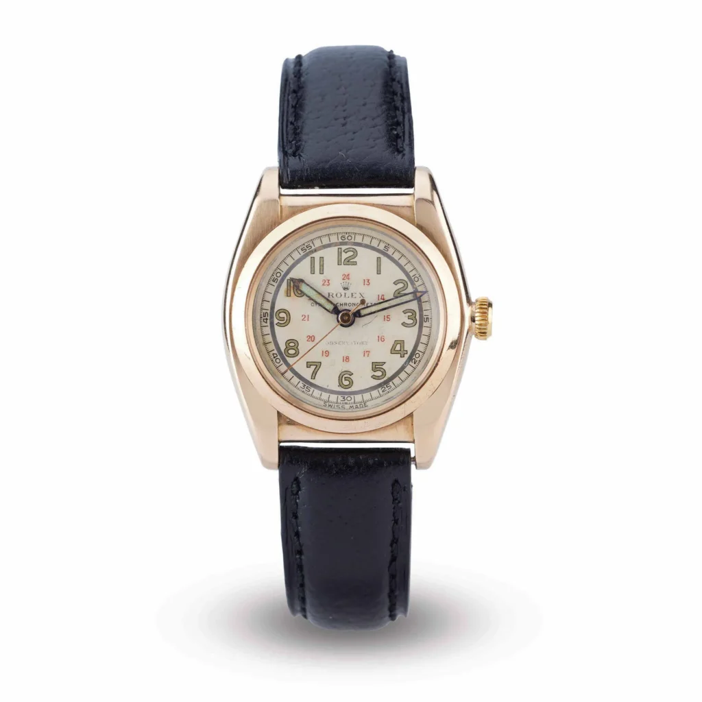A gold Rolex Oyster 3009 wristwatch with a black leather strap and a white dial displaying both 12 and 24 hour markers.