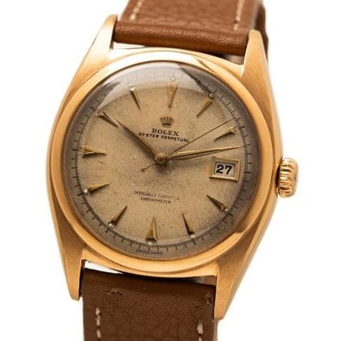 Vintage Rolex Oyster Perpetual 6074 watch featuring a gold case, brown leather strap, and date display at 3 o’clock.