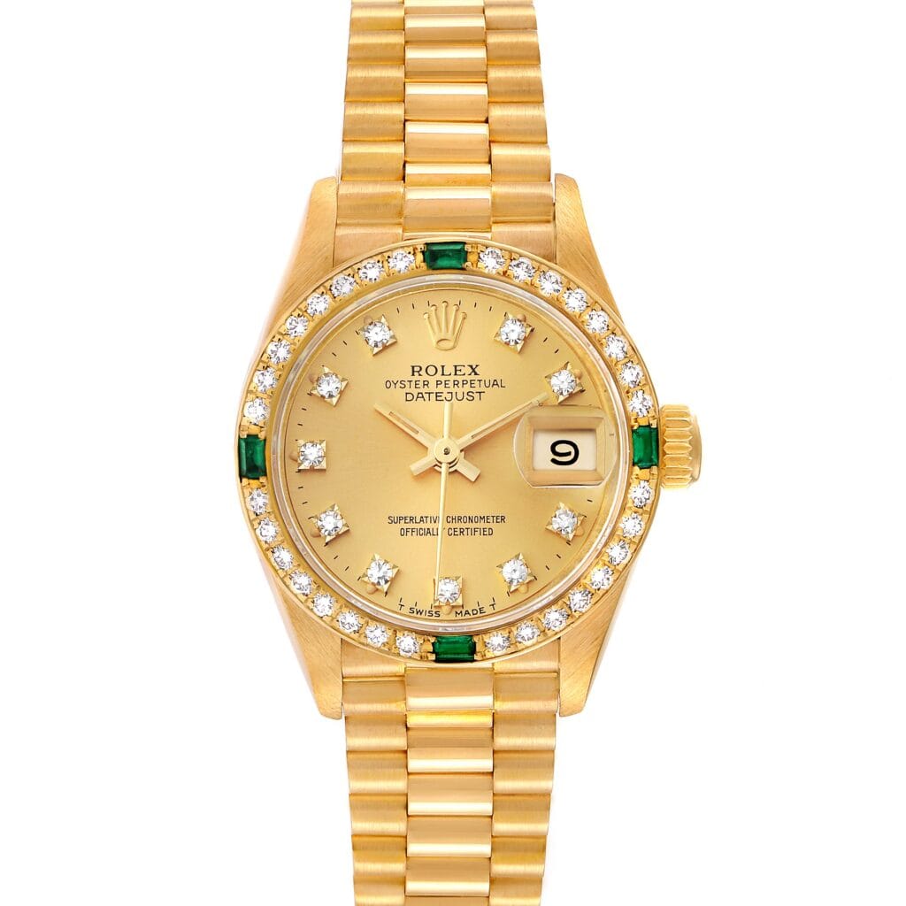 Gold Rolex Datejust 69078 watch with diamond and emerald markers, gold bracelet, and date display at 3 o’clock.
