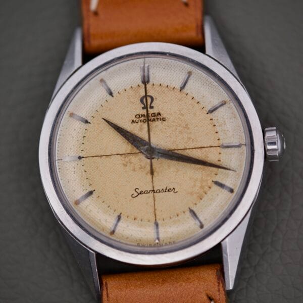 Close-up of an Omega Automatic Seamaster 2802 featuring a worn beige cross hair waffle dial and brown leather strap.