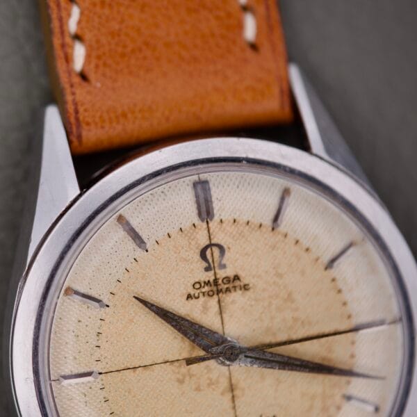 Close-up of an Omega Automatic Seamaster 2802 with a cross hair waffle dial, vintage tan leather strap, and worn off-white dial.