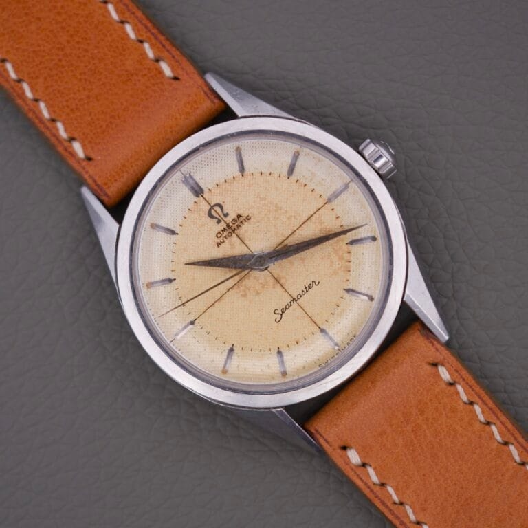 Omega Automatic Seamaster 2802 Cross Hair Waffle Dial watch with a classic tan leather strap is displayed on a gray textured surface.