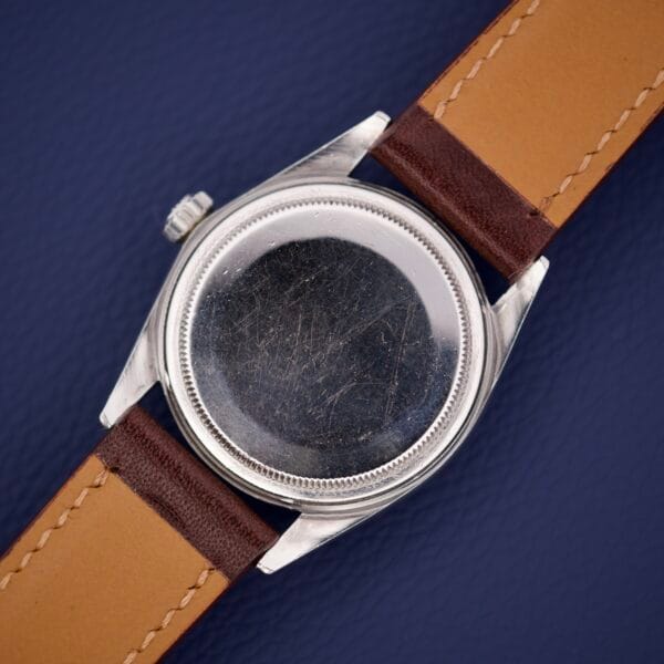 Back view of a scratched Rolex Datejust 1603 Silver Dial with Alpha hands and brown leather straps, placed on a dark blue surface.
