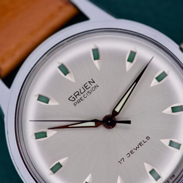 Close-up of a Gruen Precision 510 RSS wristwatch, featuring a silver dial, brown leather strap, and unique Day / Night Jump Hour Markers.