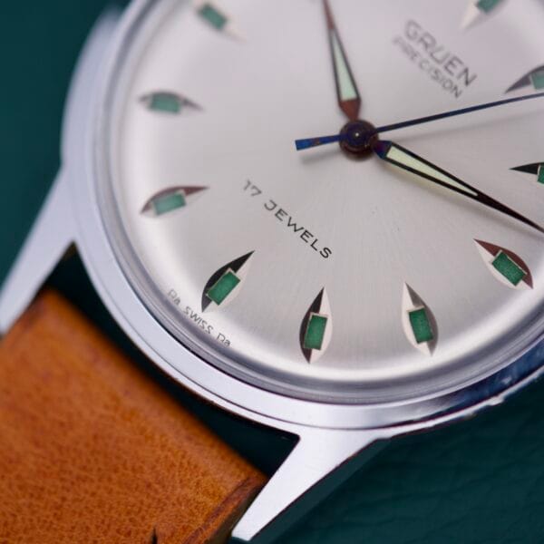 Close-up of a Gruen Precision 510 RSS wristwatch with brown leather strap and silver dial, featuring Day/Night Jump Hour markers.