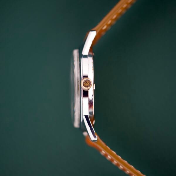 Side view of a Gruen Precision 510 RSS Day / Night Jump Hour Markers wristwatch with a brown leather strap, set against a dark green background.