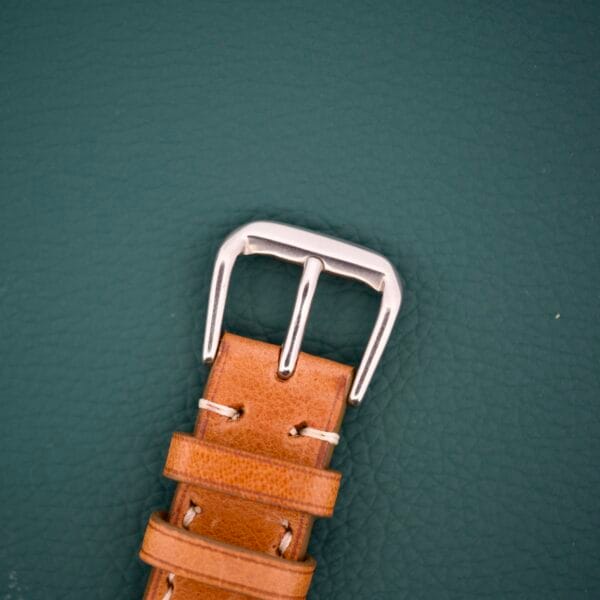 The Gruen Precision 510 RSS Day / Night Jump Hour Markers watch rests on a textured dark green background, featuring a brown leather strap with a silver buckle.