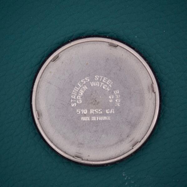Round stainless steel Gruen Precision 510 RSS Day / Night Jump Hour Markers watch back, stamped with text, displayed on a textured green surface.