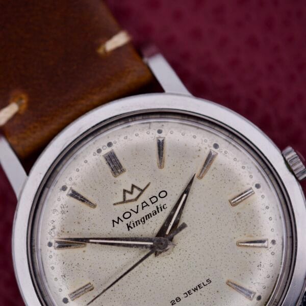 Close-up of the Movado Kingmatic Ref. 15051 28 Jewels wristwatch, featuring a speckled dial and brown leather strap.