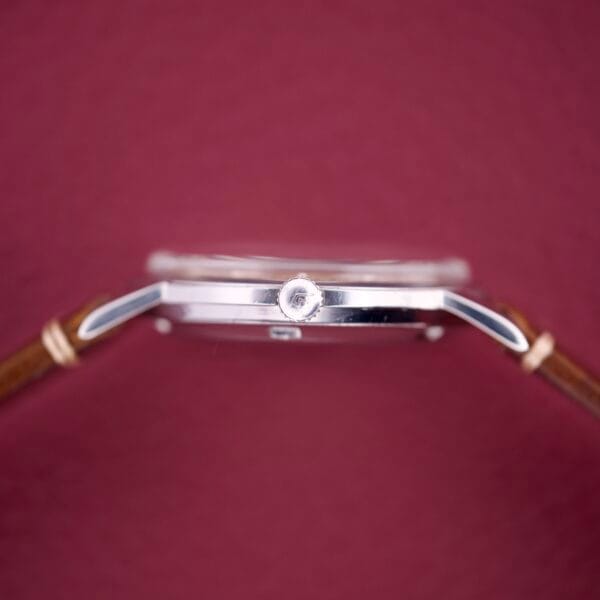 Side view of the Movado Kingmatic Ref. 15051 28 Jewels wristwatch with a brown leather strap, set against a burgundy background.
