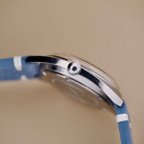 Close-up side view of the Seiko 6602-8040 Manual Wind Date Sunburst Dial wristwatch with a blue strap, set against a neutral background.