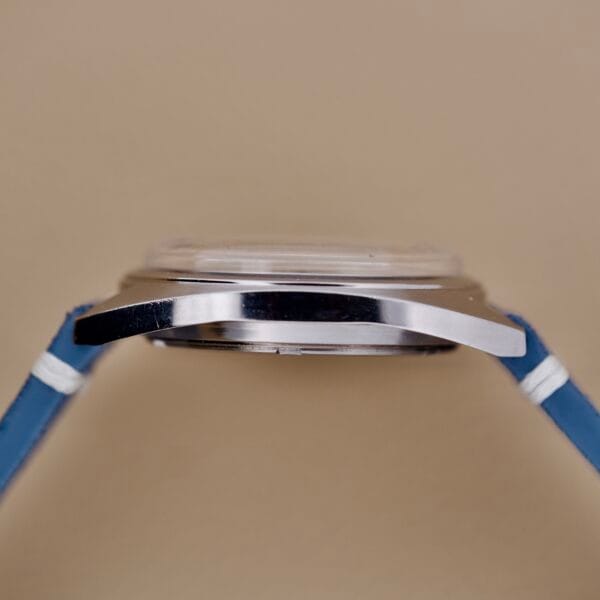 Side view of the Seiko 6602-8040 Manual Wind Date Sunburst Dial wristwatch in silver with blue straps, showcased against a beige background.