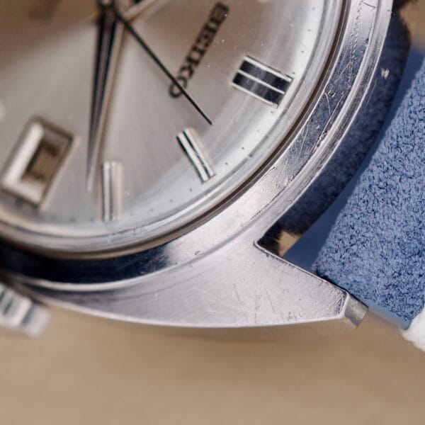 Close-up of the Seiko 6602-8040 Manual Wind Date Sunburst Dial watch face, showcasing its sunburst dial, with a blue leather strap and case scratches visible.