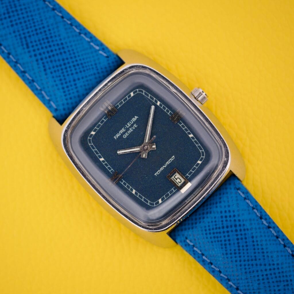 The Favre Leuba Tornado Blue Dial Automatic Date watch, featuring a blue strap and square case, rests on a yellow textured background.