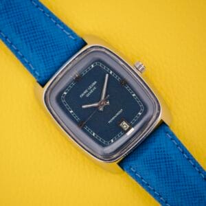 The Favre Leuba Tornado Blue Dial Automatic Date watch, featuring a blue strap and square case, rests on a yellow textured background.