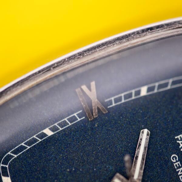 Close-up of the Favre Leuba Tornado Blue Dial Automatic Date watch face, featuring Roman numeral IX, set against a vibrant yellow background.