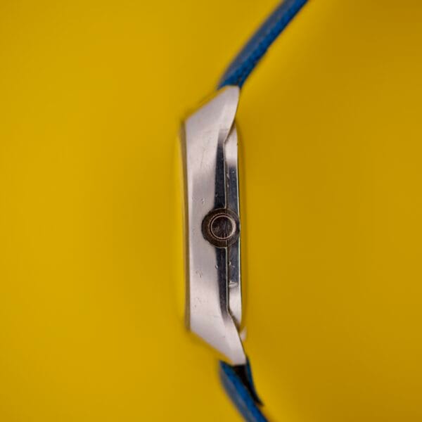Favre Leuba Tornado Blue Dial Automatic Date wristwatch, shown on its side with a blue strap, is set against a bright yellow background.