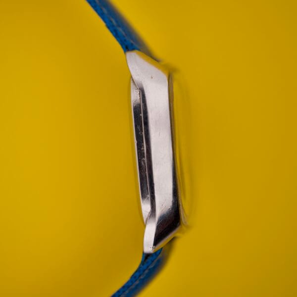 Side view of the Favre Leuba Tornado Blue Dial Automatic Date wristwatch with a blue strap, set against a solid yellow background.