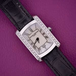 Baume & Mercier Hampton 65504 with mother-of-pearl dial, diamond-set case flanks, and black leather strap on purple background.