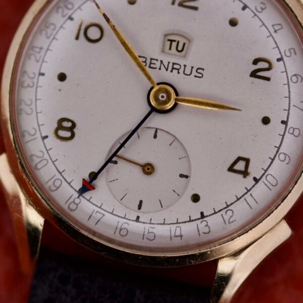 Close-up of a vintage Benrus Triple Calendar Pointer Model CE 13 watch featuring gold hands, a subdial, and a day window.