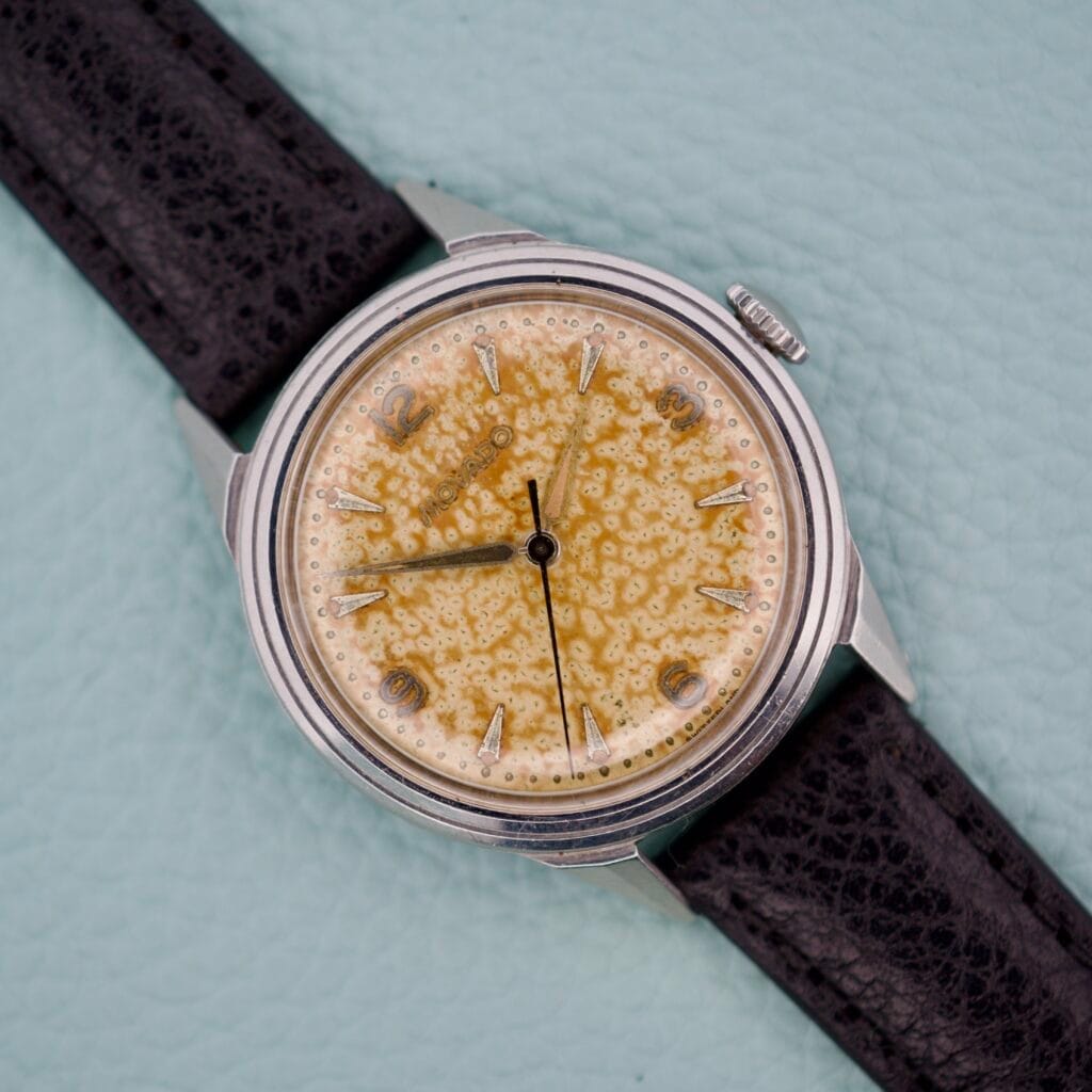 Movado Caltrava Ref. 18271 Tropic Dial Stainless Steel wristwatch featuring a textured yellow dial and black leather strap, displayed on a light blue background.