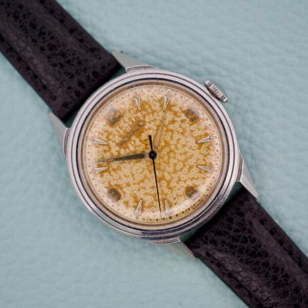 Movado Caltrava Ref. 18271 Tropic Dial Stainless Steel wristwatch featuring a textured yellow dial and black leather strap, displayed on a light blue background.