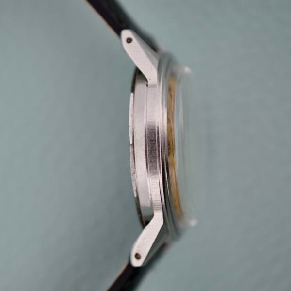 Side view of the Movado Caltrava Ref. 18271 Tropic Dial Stainless Steel wristwatch, featuring lugs and a black leather strap with refined design, set against a light background.