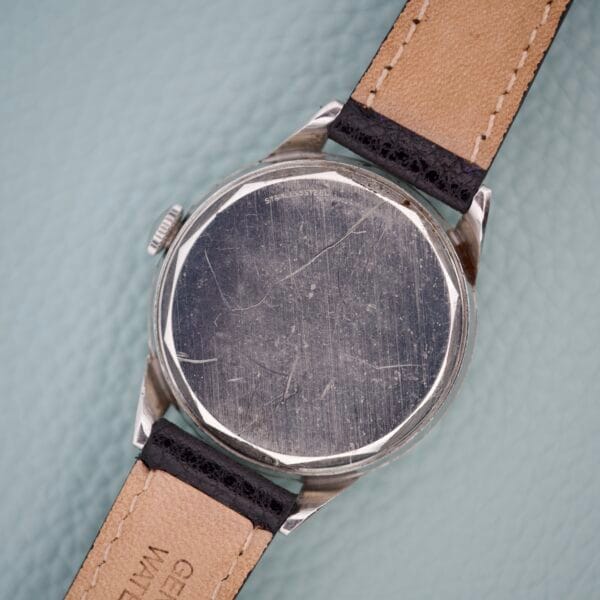 The scratched back of a Movado Caltrava Ref. 18271 Tropic Dial Stainless Steel wristwatch with a tan leather strap, resting on a light blue textured surface.
