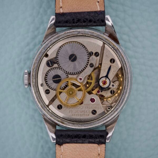 A close-up of the Movado Caltrava Ref. 18271 Tropic Dial Stainless Steel watch showcasing its mechanical movement, visible gears, and a beige leather strap.