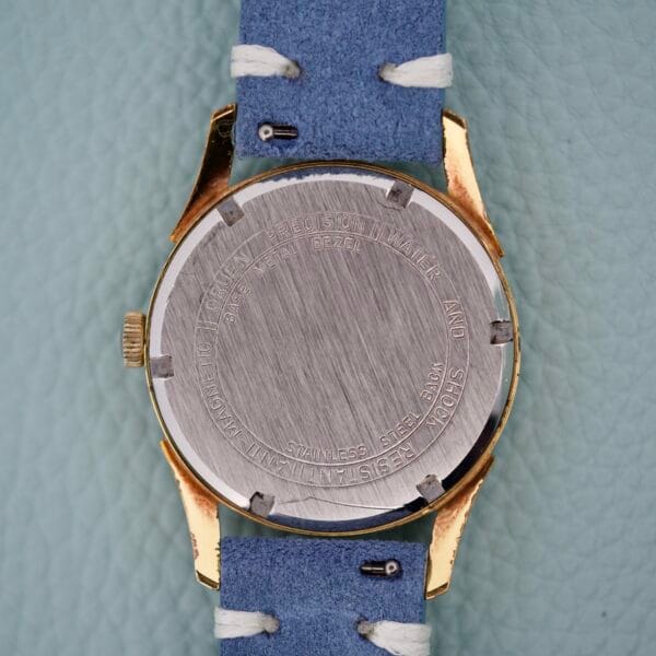 A close-up of the Gruen Precision Date 510RSS CA Sunburst Dial watch back with engraved text, paired with a blue leather strap featuring white stitching.