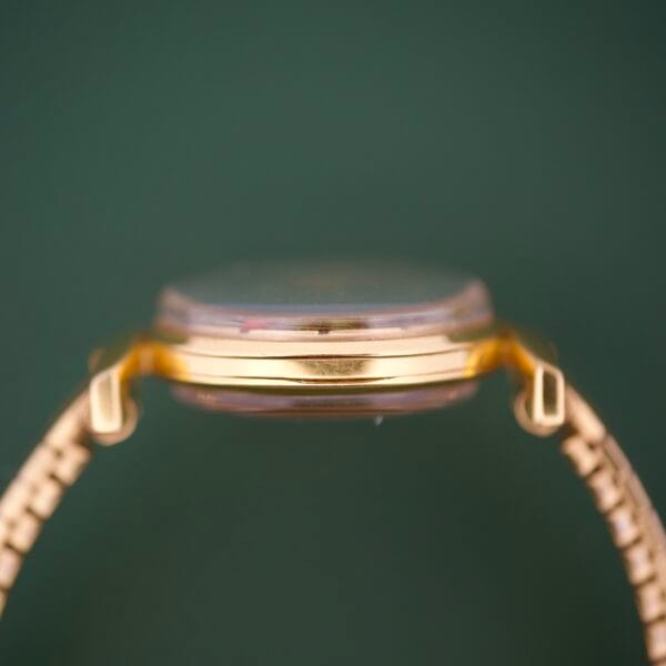 Side view of the Ernest Borel Cocktail Kaleidoscope White Dial watch with a gold case, showcased against a green background and emphasizing its thin profile.