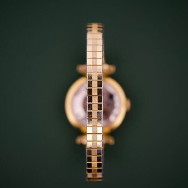 The Ernest Borel Cocktail Kaleidoscope features a white dial and square-link gold band, photographed from the side against a dark green background.