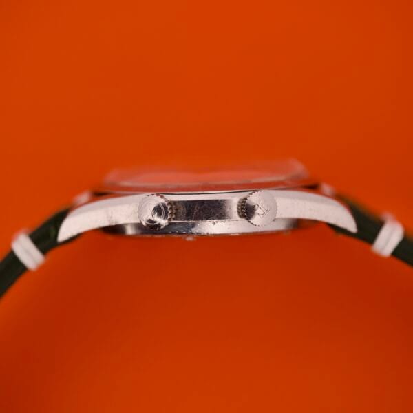 Side view of a Favre Leuba Geneve Seabird Alarm Stainless Steel watch with a green strap, displayed against an orange background.