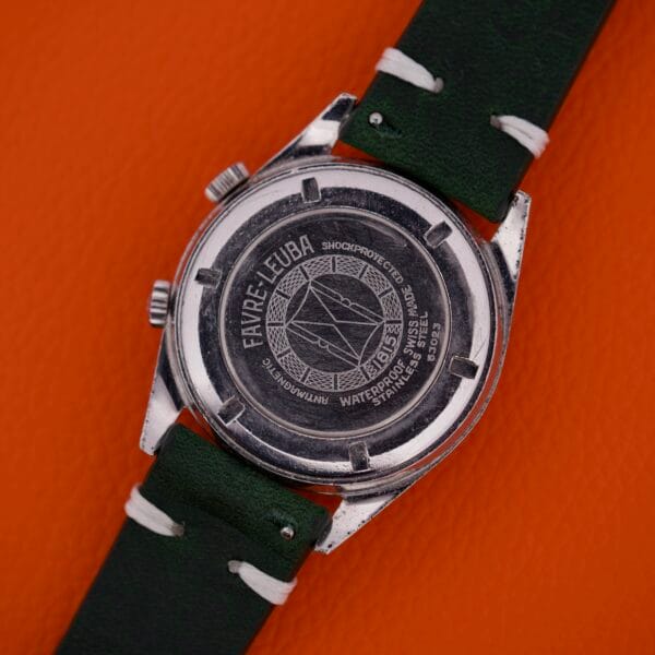 The Favre Leuba Geneve Seabird Alarm Stainless Steel watch showcases an engraved case back, green leather strap, and orange background, combining vintage style with durable stainless steel construction.
