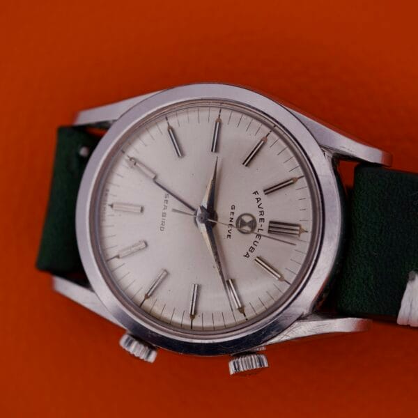 The Favre Leuba Geneve Seabird Alarm Stainless Steel wristwatch, with a white face and green strap, is shown against an orange background.
