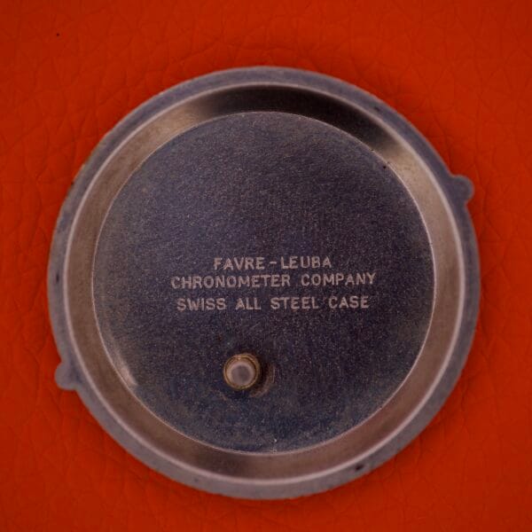 Round stainless steel back from a Favre Leuba Geneve Seabird Alarm, inscribed with FAVRE-LEUBA CHRONOMETER COMPANY SWISS ALL STEEL CASE, shown on an orange background.