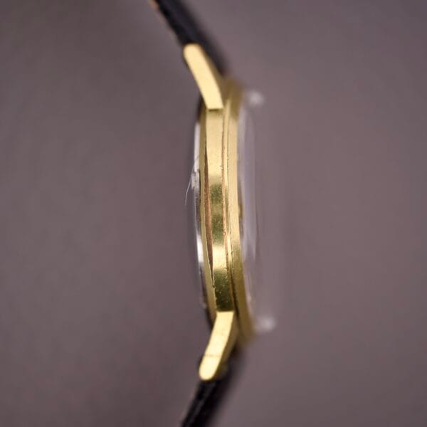 Side view of the Gruen Precision 25 Jewels Autowind Sunburst Dial, featuring a thin gold case, slightly domed glass, and black strap.