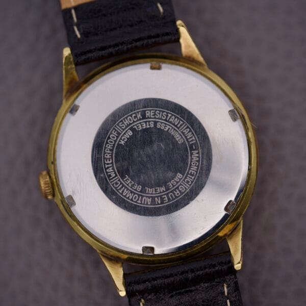 Close-up of the back of a Gruen Precision 25 Jewels Autowind Sunburst Dial wristwatch with black strap, showing engraved 25 Jewels Autowind text near the center.