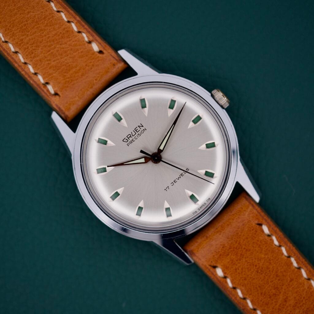 Gruen Precision 510 RSS Day/Night Jump Hour Markers wristwatch with a brown leather strap is showcased on a dark green background, echoing the timeless RSS Day/Night style.
