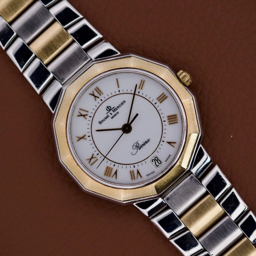 The Baume & Mercier Riviera Two-Tone Ref. 5130.038 features Roman numerals on a brown leather background, offering a classic and timeless style.