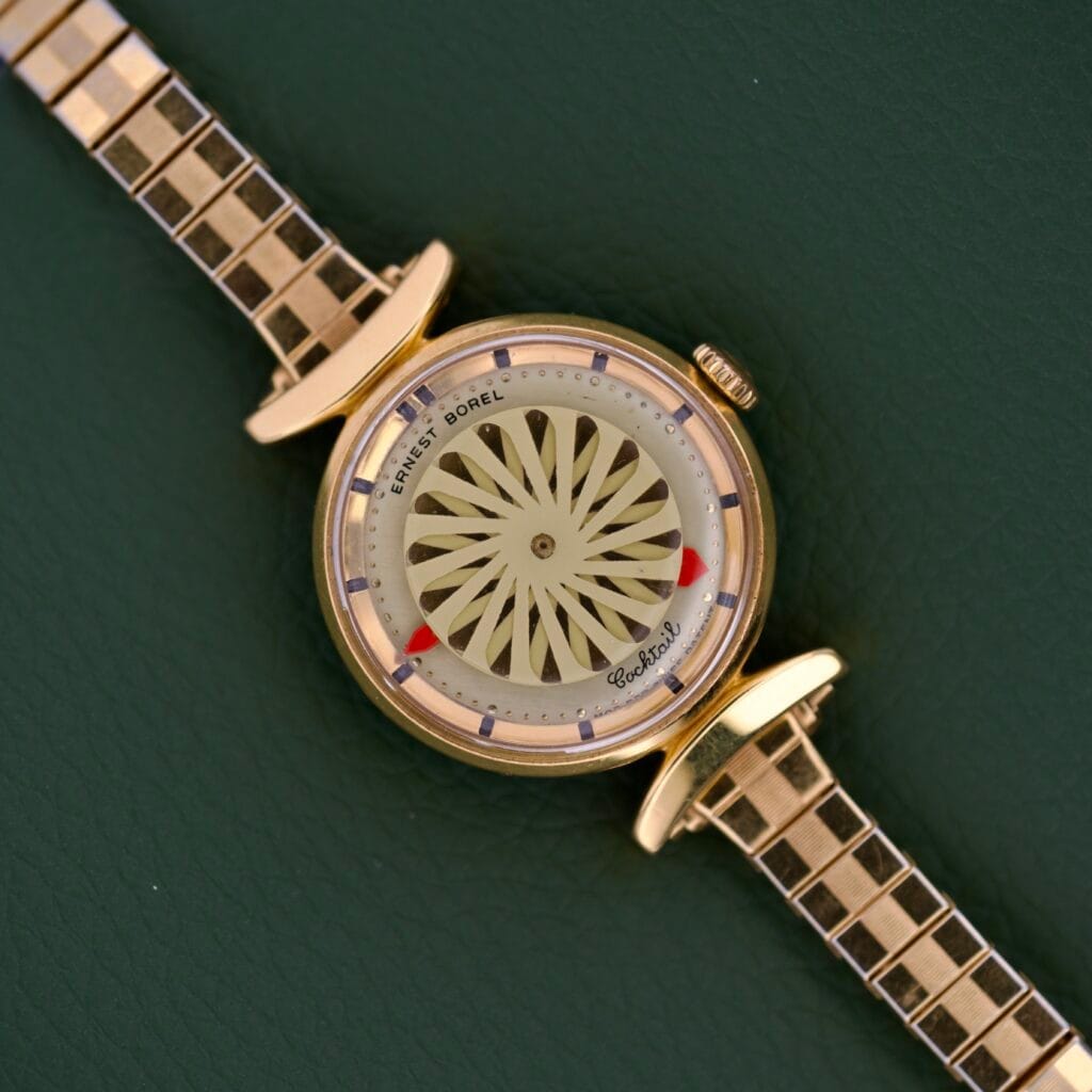 Ernest Borel Cocktail Kaleidoscope White Dial wristwatch with a distinctive patterned dial and square-link band, displayed on a green textured background.