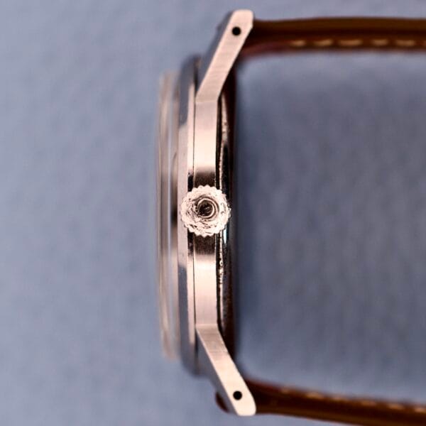 Side view of the Omega Ref. 2271-2 Jumbo Stainless Steel Case 30T2 wristwatch with a brown leather strap and textured crown, highlighting its case against a light textured background.