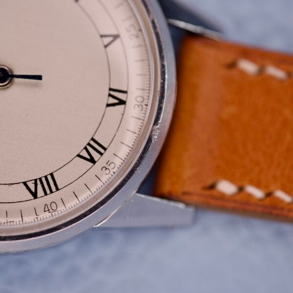 Close-up of an Omega Ref. 2271-2 Jumbo Stainless Steel Case 30T2 watch face with Roman numerals and a brown leather strap on a light blue surface, showcasing its classic design.